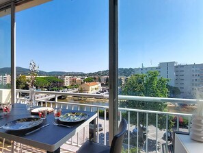 A balcony with a table set for dining, overlooking a cityscape with buildings and greenery. - Bel Horizon 2 by Interhome (Sainte Maxime)
