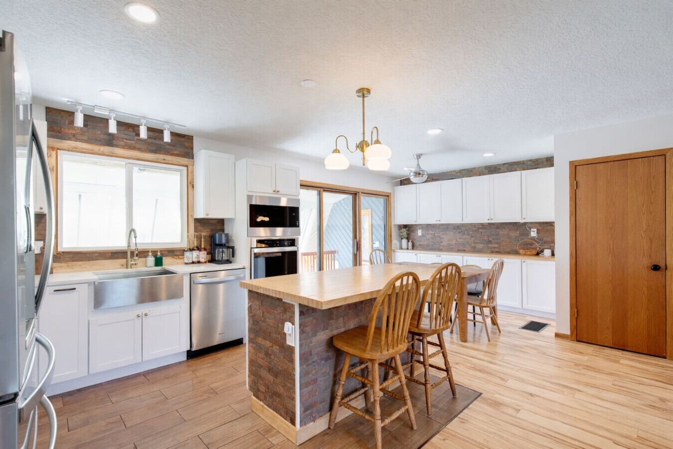 A modern kitchen with white cabinets, a central island with chairs, stainless steel appliances, and a wooden floor.