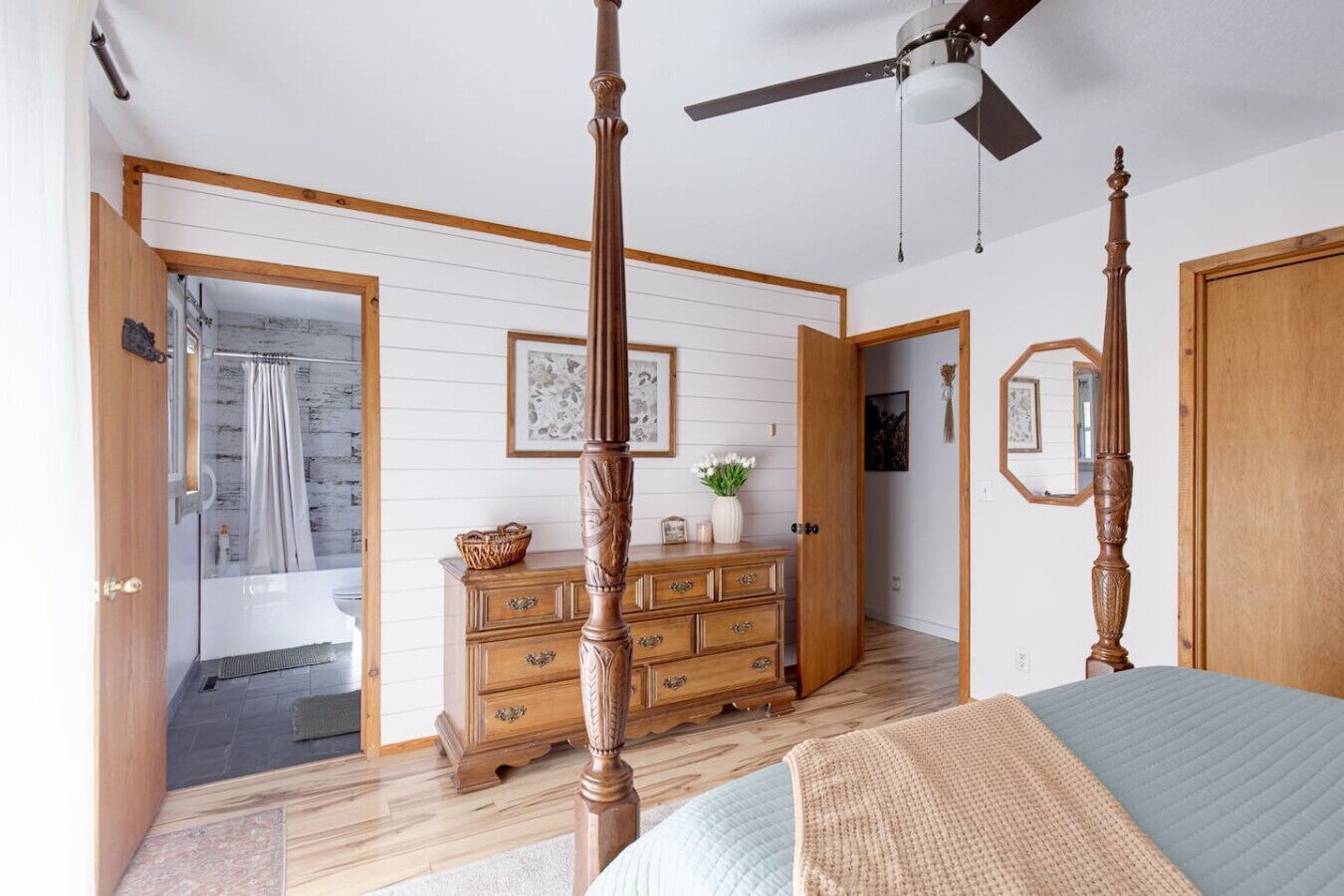 A bedroom with a four-poster bed, wooden dresser, and a ceiling fan.