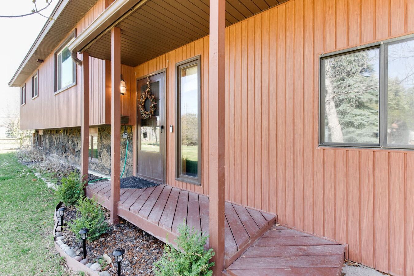 Une maison en bois avec un porche, une porte d’entrée et une grande fenêtre.