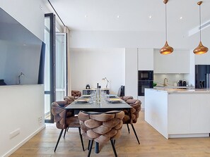 Eine moderne Küche mit Kochinsel, Pendelleuchten und einem Essbereich mit langem Tisch und Polsterstühlen.
