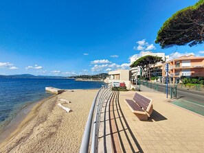 Eine Uferpromenade mit einer Bank, freier Blick auf das Meer und Gebäuden im Hintergrund.