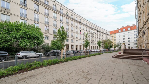 Un edificio a più piani con una fila di auto parcheggiate lungo la strada.