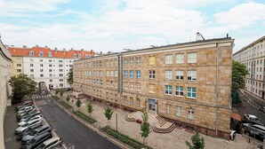Un edificio a più piani con una fila di auto parcheggiate davanti, cielo sereno e un percorso pedonale.