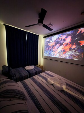 Un dormitorio con cama, almohadas, ventilador de techo y televisor mostrando una imagen de peces.
