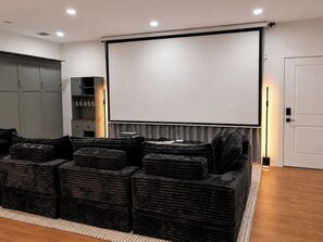 Ein Heimkino mit großer Leinwand, schwarzen, gepolsterten Sitzgelegenheiten, einem Schrank mit Weingläsern und einer Tür.