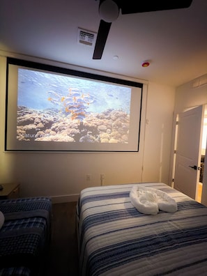 Ein Hotelzimmer mit einem Bett, einem an der Wand befestigten Projektor, der eine Unterwasserwelt zeigt, einem Deckenventilator und einer Tür.