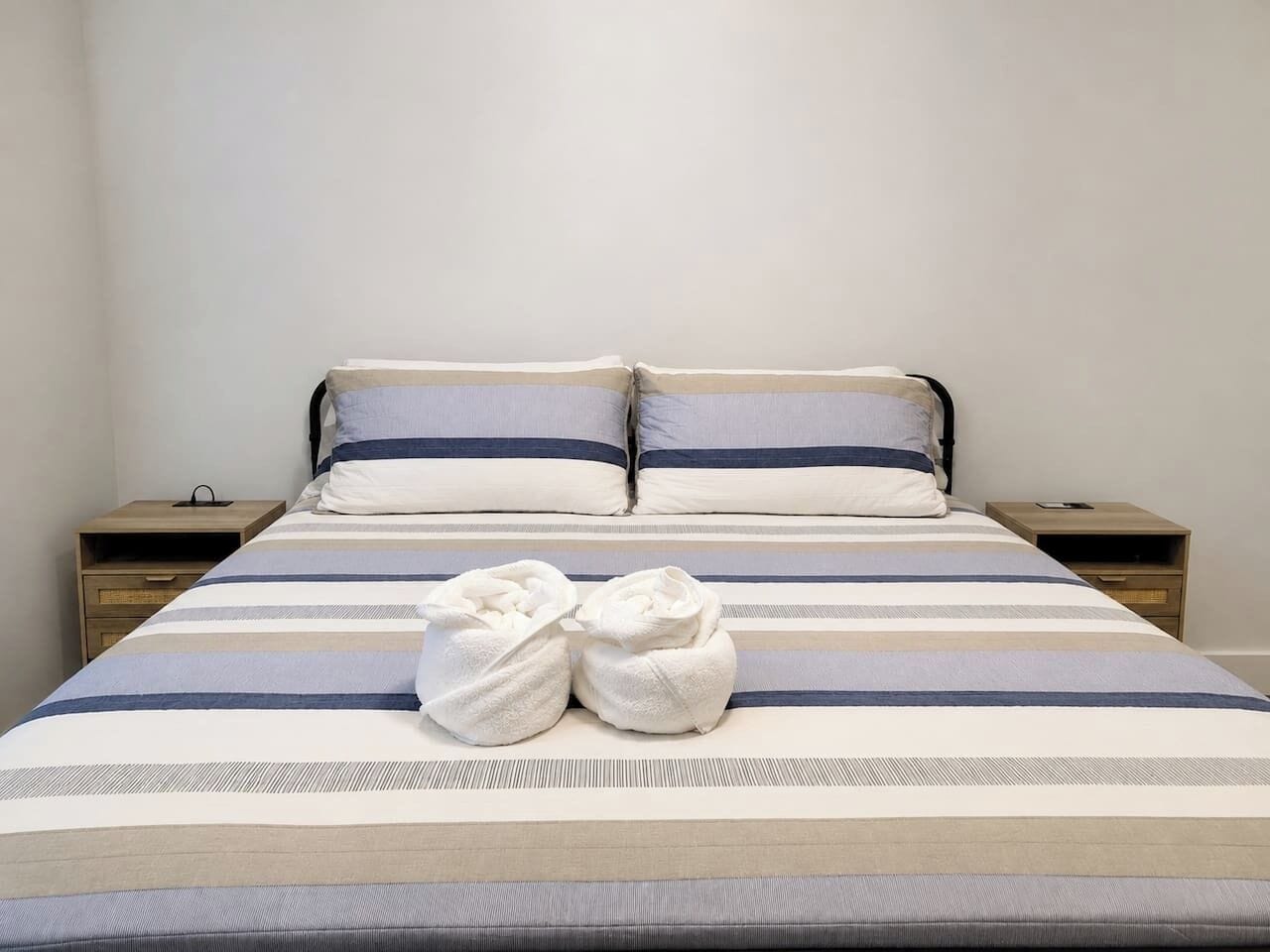Ein ordentlich bezogenes Bett mit gestreifter Bettwäsche, zwei Kissen und zwei Handtüchern.