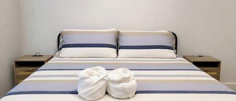Ein ordentlich bezogenes Bett mit gestreifter Bettwäsche, zwei Kissen und zwei Handtüchern.