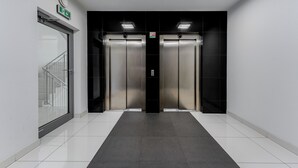 Un vestíbulo de ascensores moderno con dos ascensores, una puerta de vidrio y una pared negra.