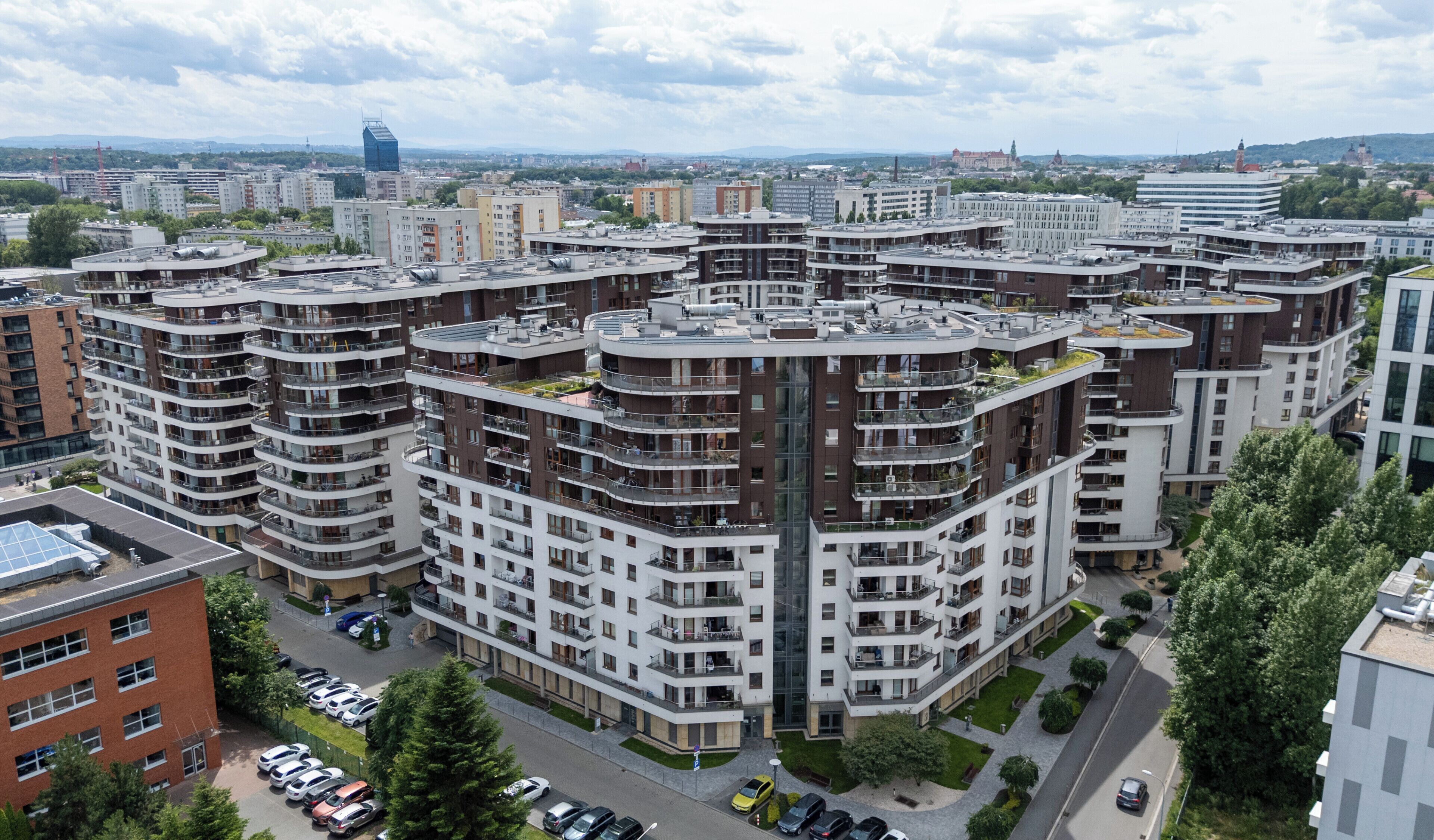 Un edificio residencial alto con varios balcones, un estacionamiento y vistas del paisaje urbano circundante.
