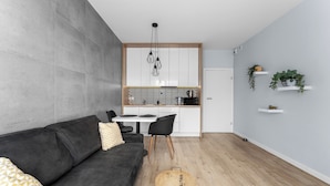 Una sala de estar moderna con un sofá gris, una mesa de centro redonda y una cocina al fondo.
