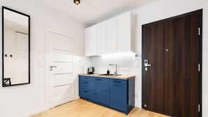A modern kitchen with white cabinets, a blue countertop, and a dark wooden door. - Warta River Esencja Apartment (Poznań)