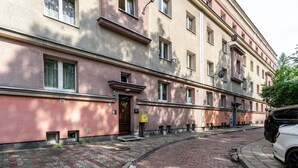 A multi-story building with a pink facade, multiple windows, and a visible entrance with a door and a small window above it. - Koszalińska Comfort Stay Apartment (Katowice)
