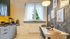 A compact kitchen with a dining area, a window with curtains, and wall-mounted artwork. - Koszalińska Comfort Stay Apartment (Katowice)