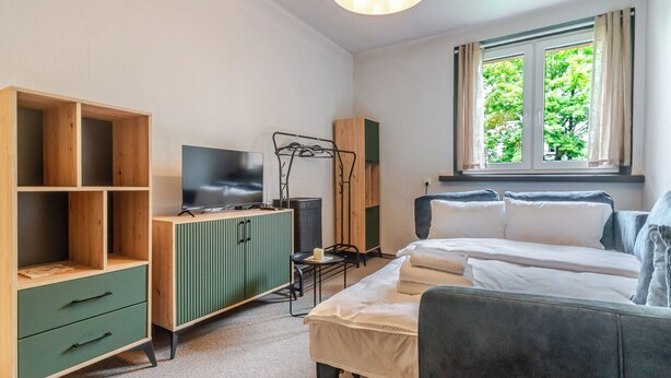 A bedroom with a bed, a TV, a wardrobe, a desk, and a window with a view of trees. - Koszalińska Comfort Stay Apartment (Katowice)