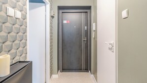 A hallway with a geometric-patterned wall, a dark door with a red sign, and a white wall with a light switch. - Koszalińska Comfort Stay Apartment (Katowice)