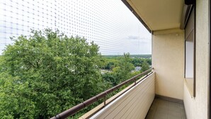 A balcony with a view of a green tree and a distant building. - Zawodzie Homely Apartment (Katowice)