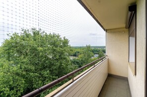 Ein Balkon mit Blick auf einen grünen Baum und ein entferntes Gebäude.