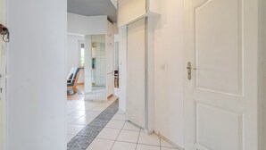 A hallway with white doors, a tiled floor, and a chair in the background. - Zawodzie Homely Apartment (Katowice)