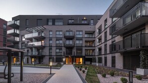 Ein modernes Mehrgeschosshaus mit Balkonen, einem zentralen Eingang und einem gepflasterten Weg.