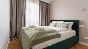 Ein ordentlich bezogenes Bett mit einem grünen Kopfteil, einem grauen Vorhang und einer weißen Wand mit einer Steckdose.