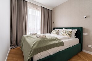 A neatly made bed with a green headboard, a grey curtain, and a white wall with a power outlet. - Nadmotławie Riverside Prestige Apartment (Gdańsk)