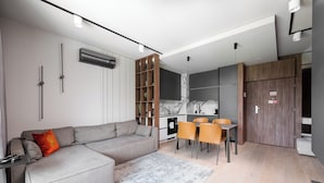Un salon moderne avec un canapé gris, une table à manger avec des chaises et un coin cuisine.