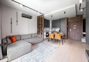 Ein modernes Wohnzimmer mit grauem Sofa, einem Esstisch mit Stühlen und einer Küchenzeile.