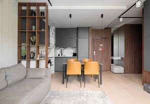 Ein modernes Wohnzimmer mit einer Couch, einem Esstisch, Stühlen, einem Bücherregal und einer Küchenzeile.