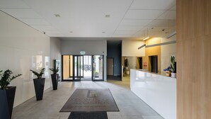Un hall d’hôtel moderne avec un comptoir d’accueil, des plantes en pot et une sortie clairement indiquée.