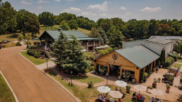 A rural setting with a building featuring a green roof, outdoor seating with umbrellas, and a prominent compass symbol on the front. - Spacious 3bd/3ba Rooftop w/Downtown Views* Garage! (Nashville)