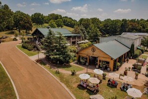 A rural setting with a building featuring a green roof, outdoor seating with umbrellas, and a prominent compass symbol on the front. - Spacious 3bd/3ba Rooftop w/Downtown Views* Garage! (Nashville)