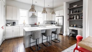 A modern kitchen with a central island, pendant lighting, and a dining area with a red chair. - Spacious 3bd/3ba Rooftop w/Downtown Views* Garage! (Nashville)