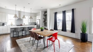 A modern kitchen with a central island, pendant lighting, and a dining area with a wooden table and red chairs. - Spacious 3bd/3ba Rooftop w/Downtown Views* Garage! (Nashville)