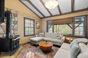 Ein Wohnzimmer mit Kamin aus Stein, einem Ecksofa und großen Fenstern.