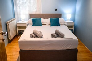 A neatly made bed with two rolled towels, a white duvet, and two pillows, one blue and one white, in a room with a wooden floor and a radiator. - Villa with swimming pool and hot tub (Metković)
