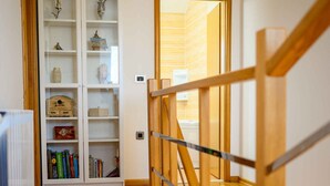 Eine Holztreppe führt zu einer Plattform mit einem weißen Bücherregal, das mit verschiedenen Gegenständen gefüllt ist.