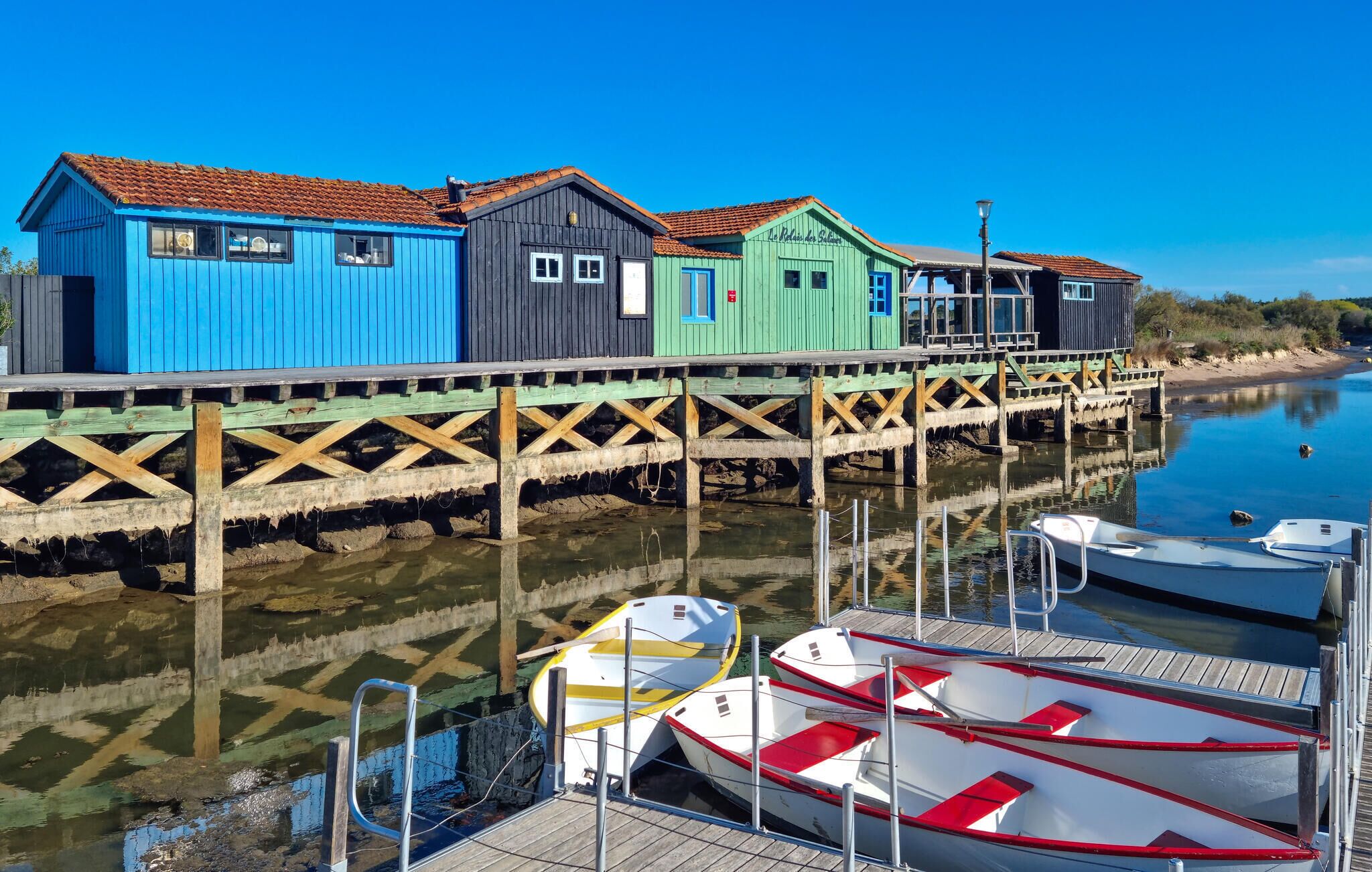 Un quai bordé de bâtiments en bois aux couleurs vives, une étendue d’eau calme et des bateaux.