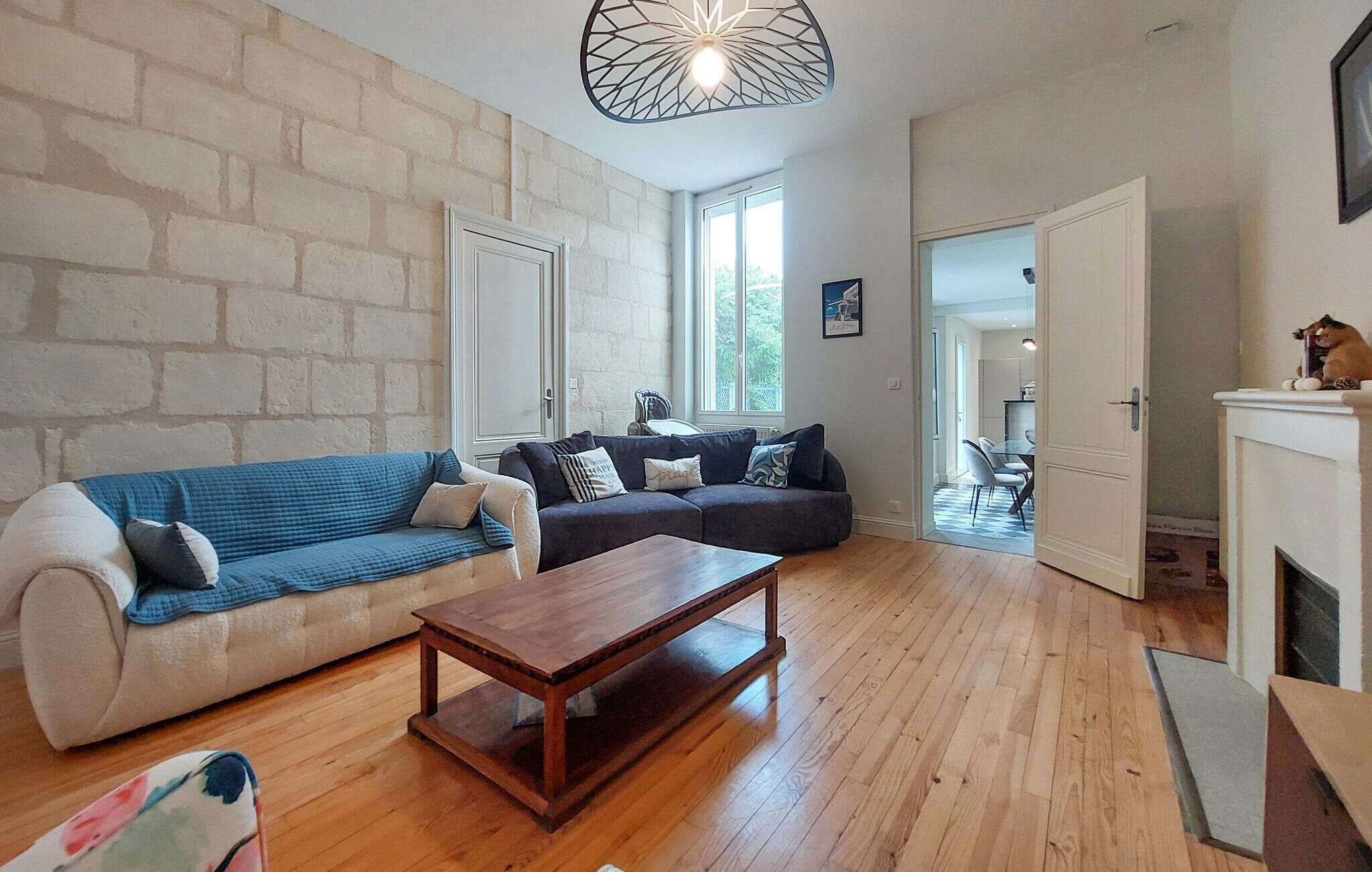 Un salon avec un mur en briques blanches, un canapé bleu, un canapé foncé, une table basse en bois et une cheminée.
