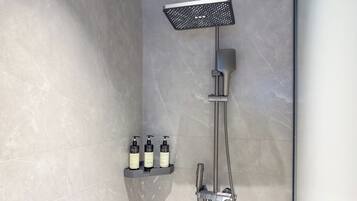 A modern shower with a handheld showerhead, a rain showerhead, and a handheld faucet. There are three bottles of shampoo on a shelf below the shower.