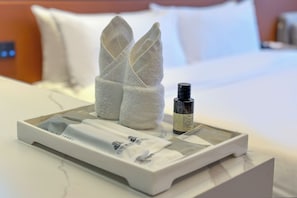 A neatly arranged dental kit on a tray, a bottle of mouthwash, and two folded towels on a hotel bed.