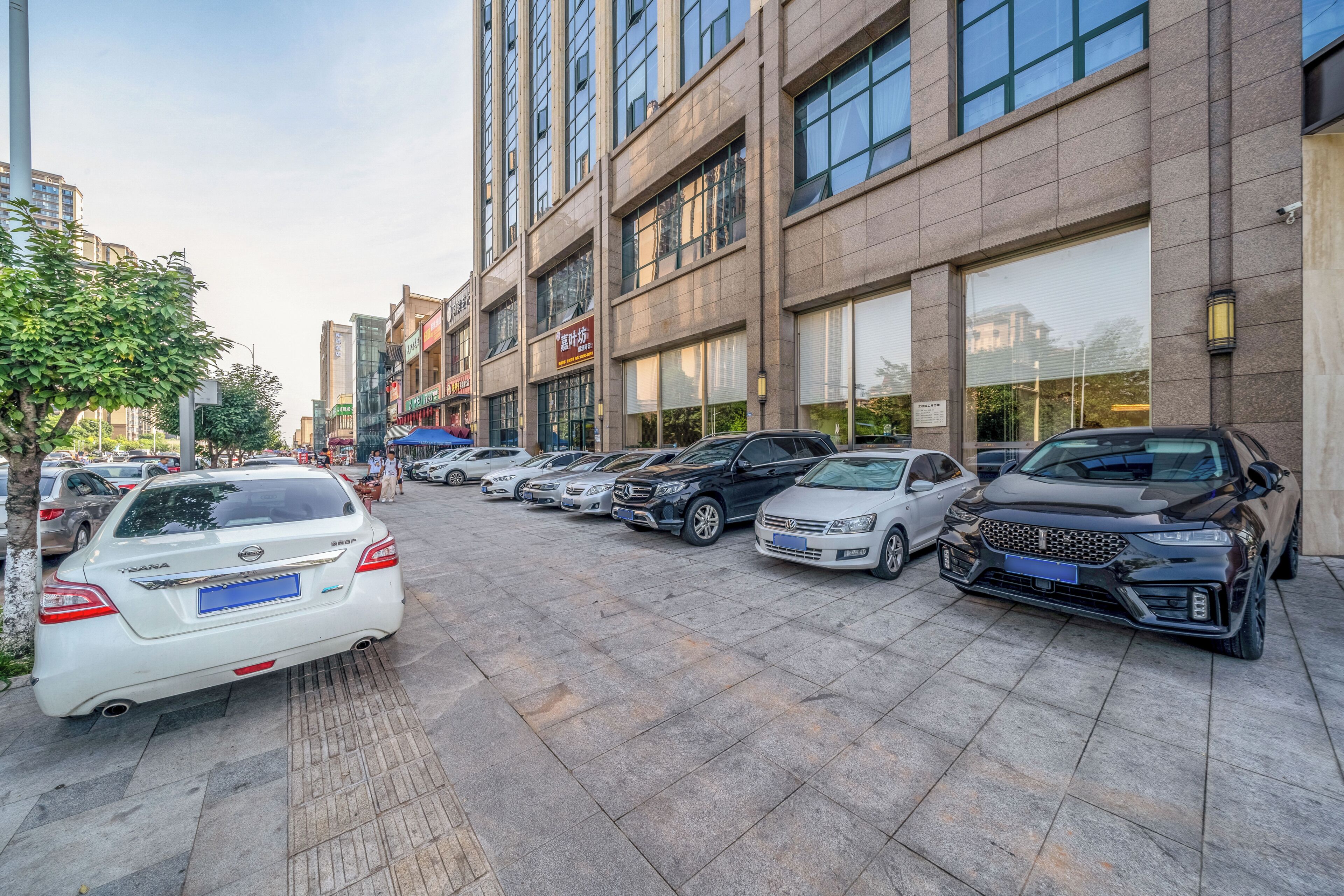 A parking lot with multiple cars, a building with large windows, and a tree on the left.