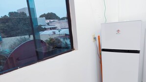 A kitchen with a white refrigerator, a window with a view of buildings, and a broom leaning against the wall.