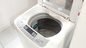 A front-loading washing machine with a control panel, a transparent door, and a small window above it.