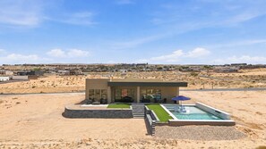 A modern house with a swimming pool, a patio, and a view of a desert landscape.