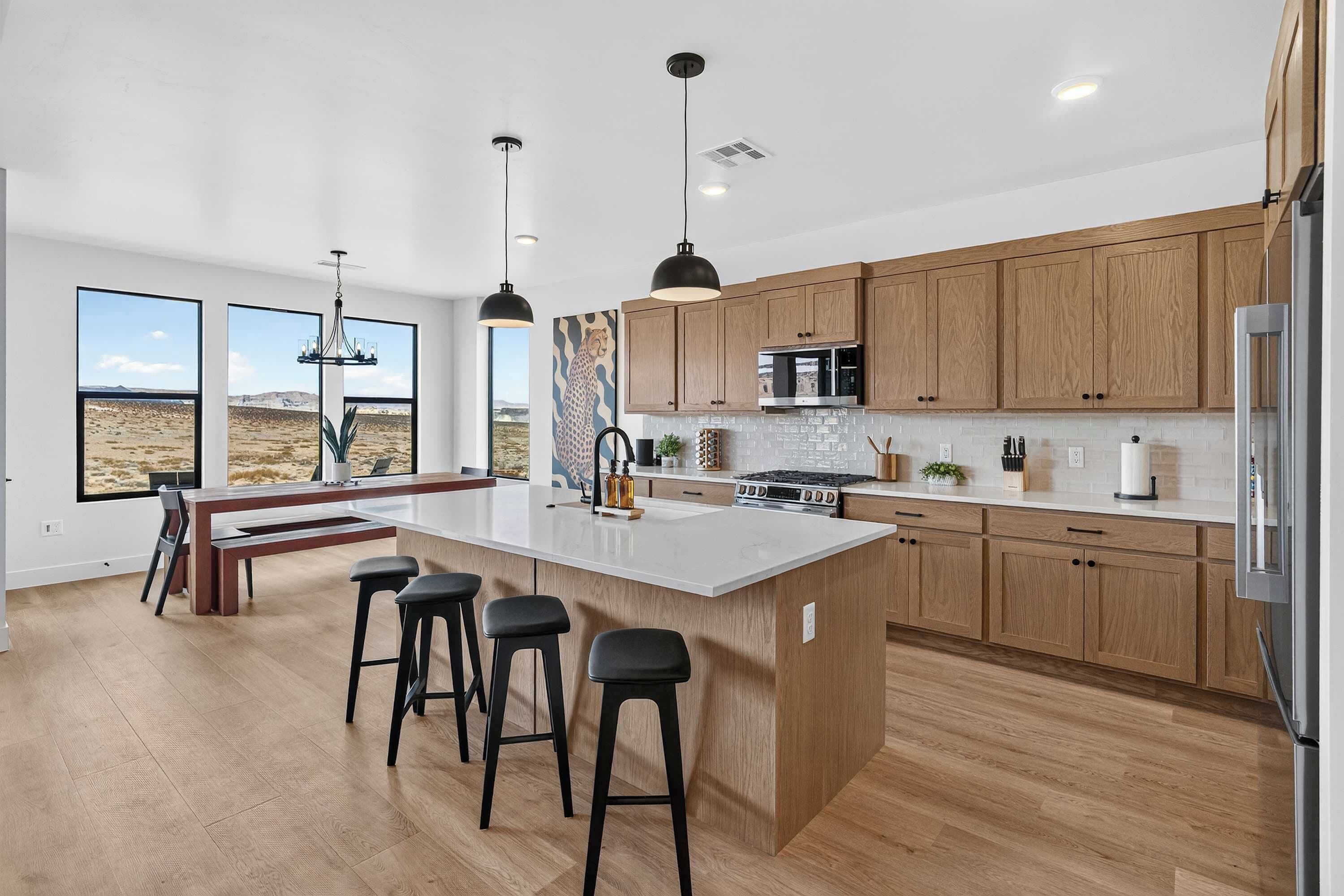 Une cuisine moderne avec des meubles en bois, un grand îlot central doté de tabourets, un éclairage suspendu et une vue sur le désert grâce à de grandes fenêtres.