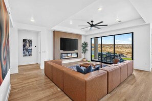 A modern living room with a large sectional sofa, a flat-screen TV, a fireplace, and a large window offering a desert view.