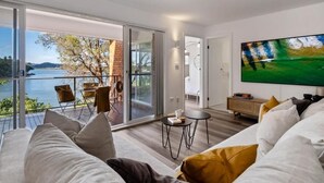 A modern living room with a large TV, a sofa, and a balcony with a view of the water.