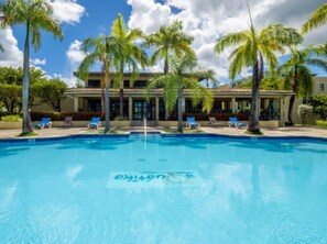 A swimming pool with lounge chairs and palm trees, surrounded by a building with a tiled roof. - Aquatika Villa 5103 - Water Park Beach Getaway in Loíza (Loíza)